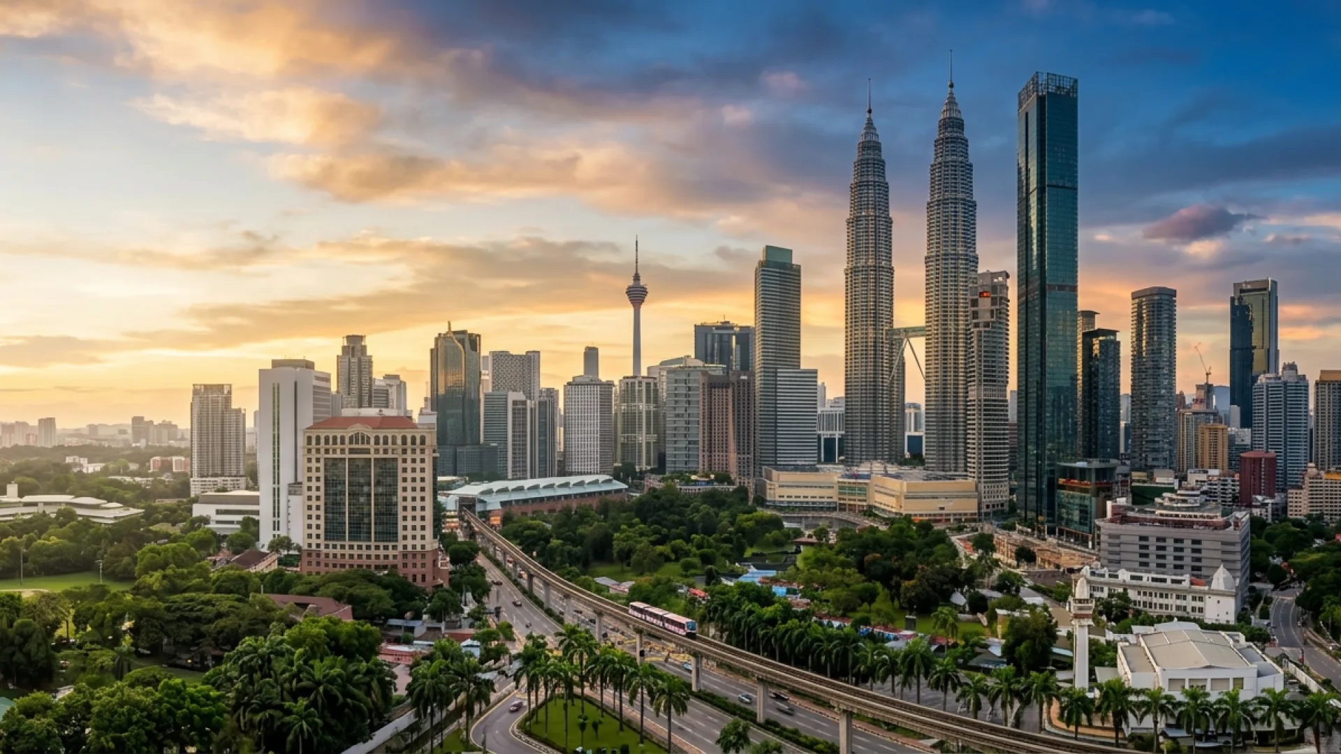 The Kuala Lumpur skyline at sunset, with the Petronas Twin Towers and KL Tower above the rail line and treetops